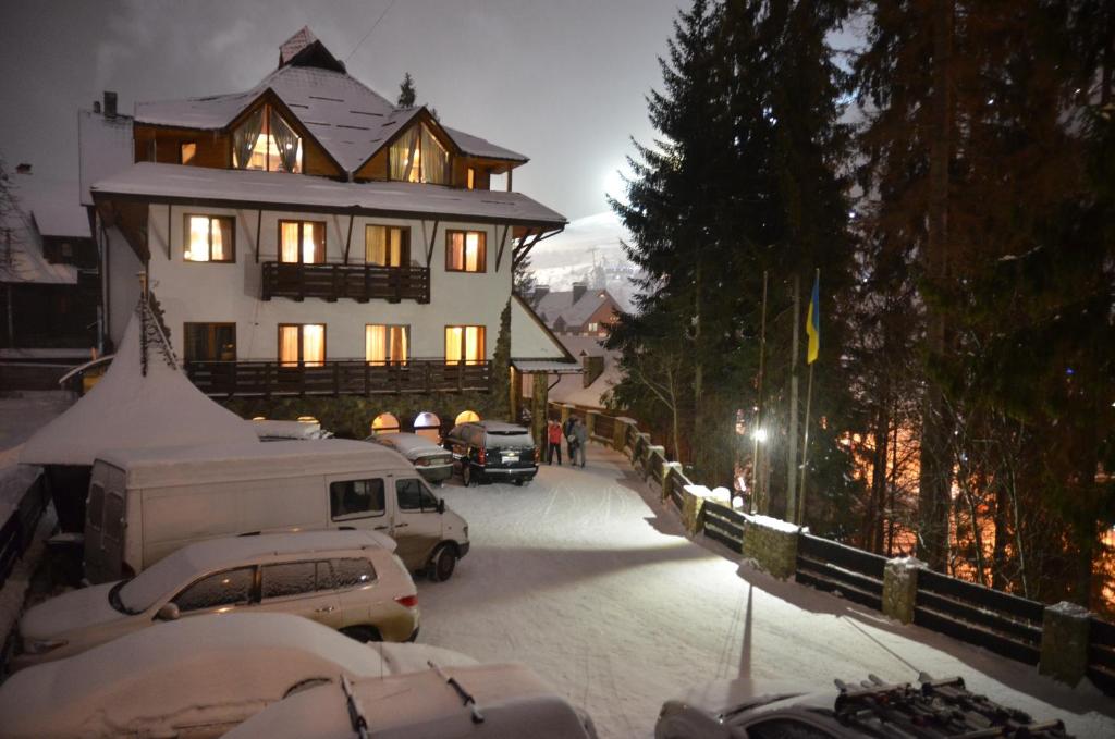 a snow covered street with a large house and cars at Chaban Aparthotel in Bukovel