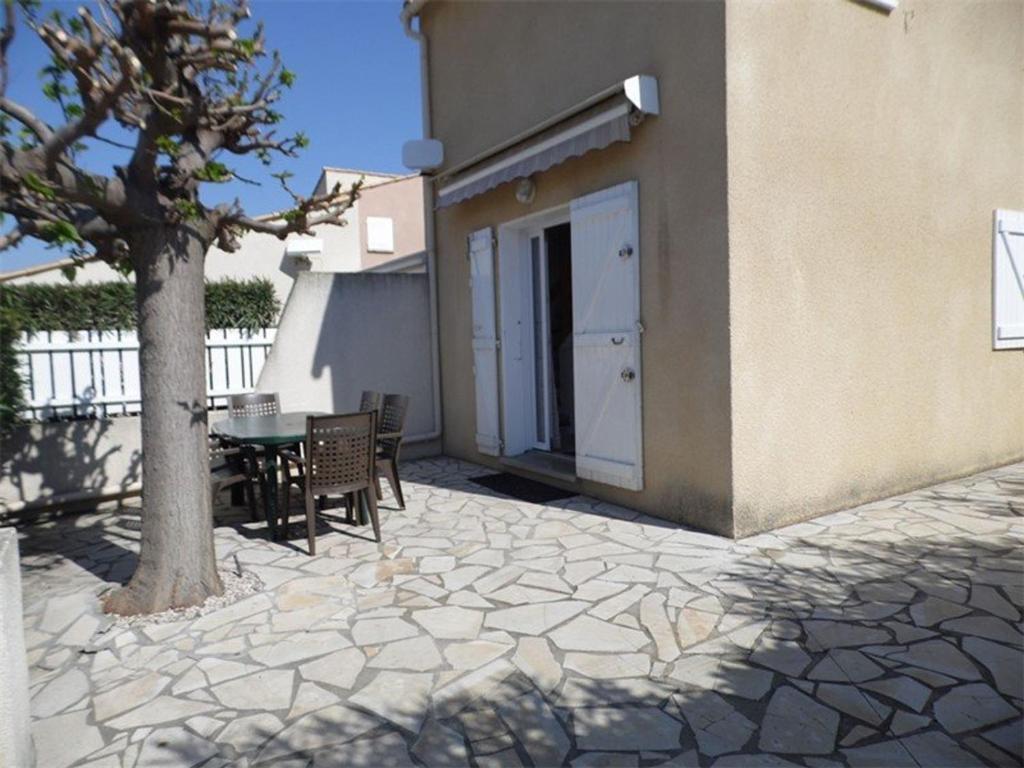 un patio con tavolo e albero accanto a un edificio di Maison Marseillan-Plage, 3 pièces, 6 personnes - FR-1-326-397 a Marseillan