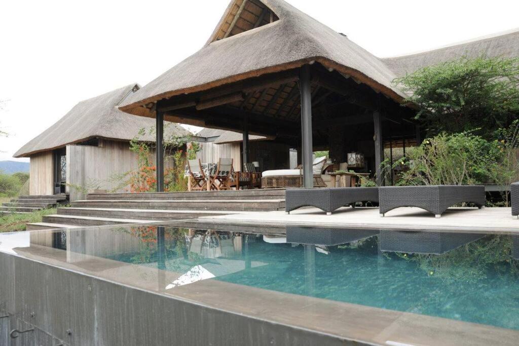 a house with a thatched roof and a swimming pool at Imvubu Lodge, Royal Jozini PGR, eSwatini in Lavumisa