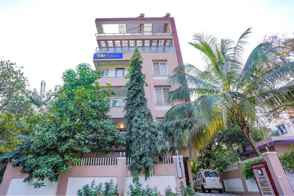 un edificio rosa alto con árboles delante de él en FabHotel Rudra Residency en Chinchiwad