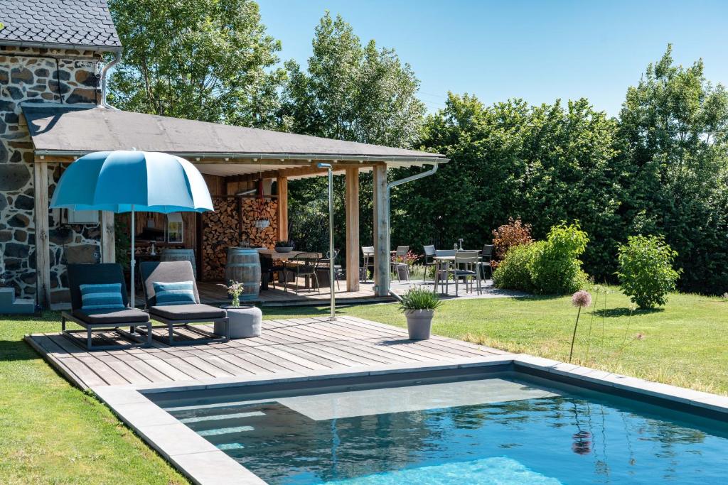 a swimming pool with an umbrella next to a house at MAISON de la Bonne Vie in Thérondels