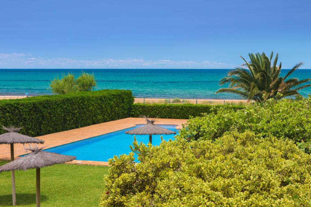 a swimming pool with umbrellas in front of the ocean at Las Dunas 02 in Denia