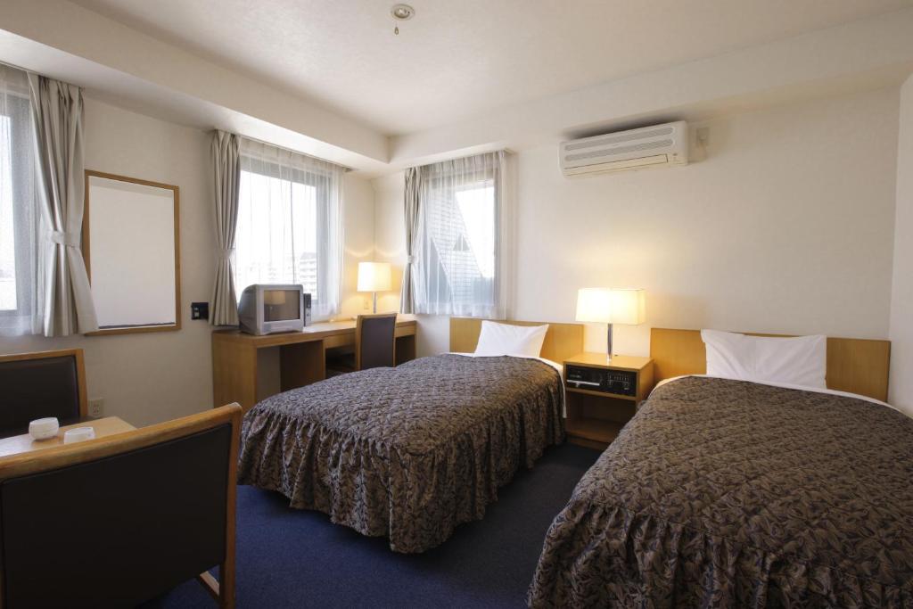 a hotel room with two beds and a television at Sankei City Hotel Hachioji in Hachioji