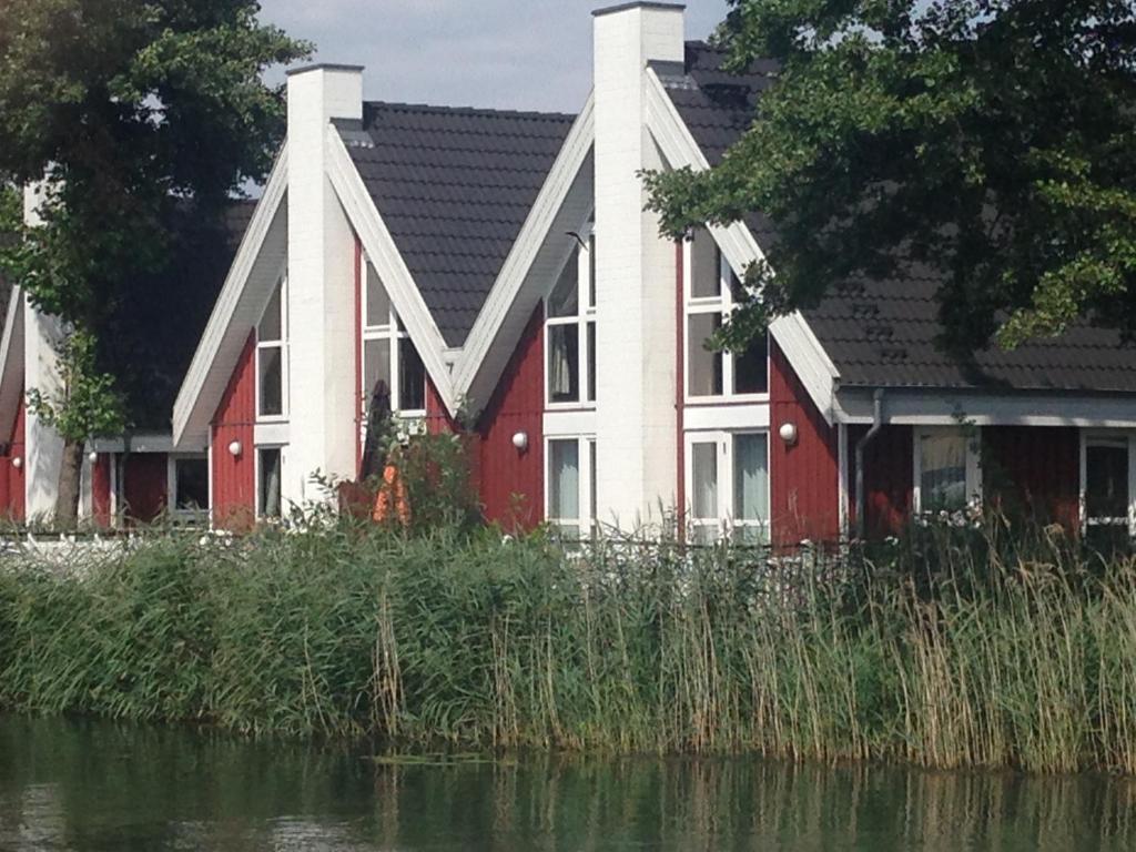una casa roja y blanca junto a un cuerpo de agua en Ferienhaus mit Wasserterrasse - mit Sauna und Kamin - inklusive Nebenkosten, en Wendisch Rietz