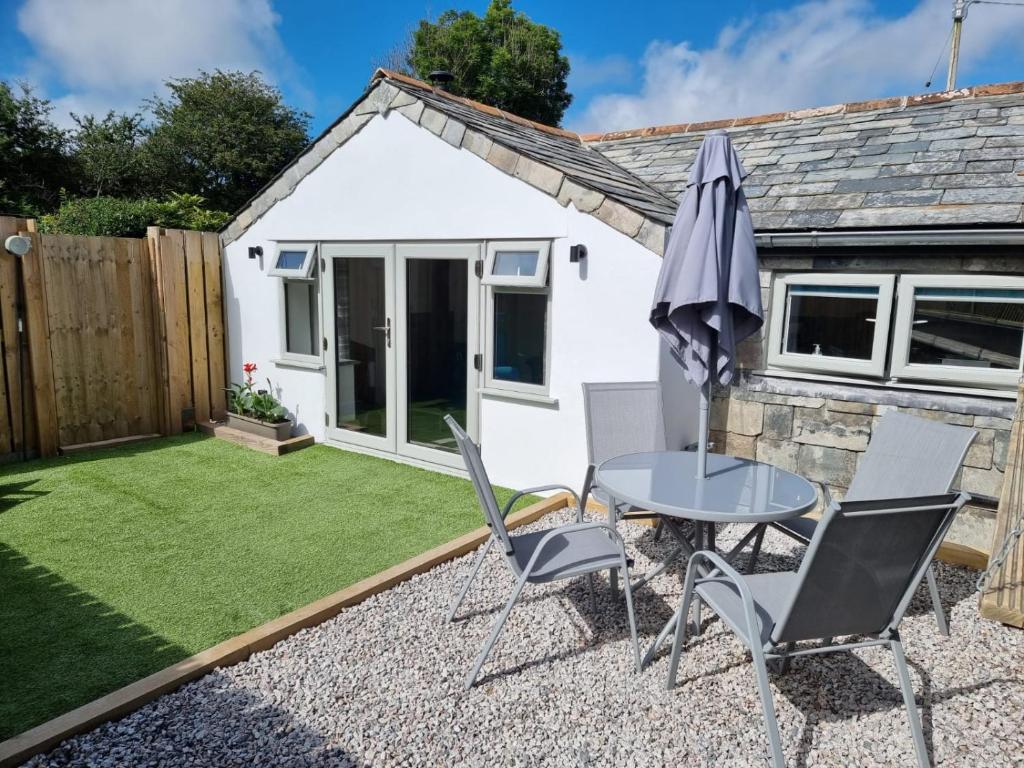 a small garden with a table and chairs and an umbrella at The Old Pottery 2 Person Dog Friendly Cottage in Delabole