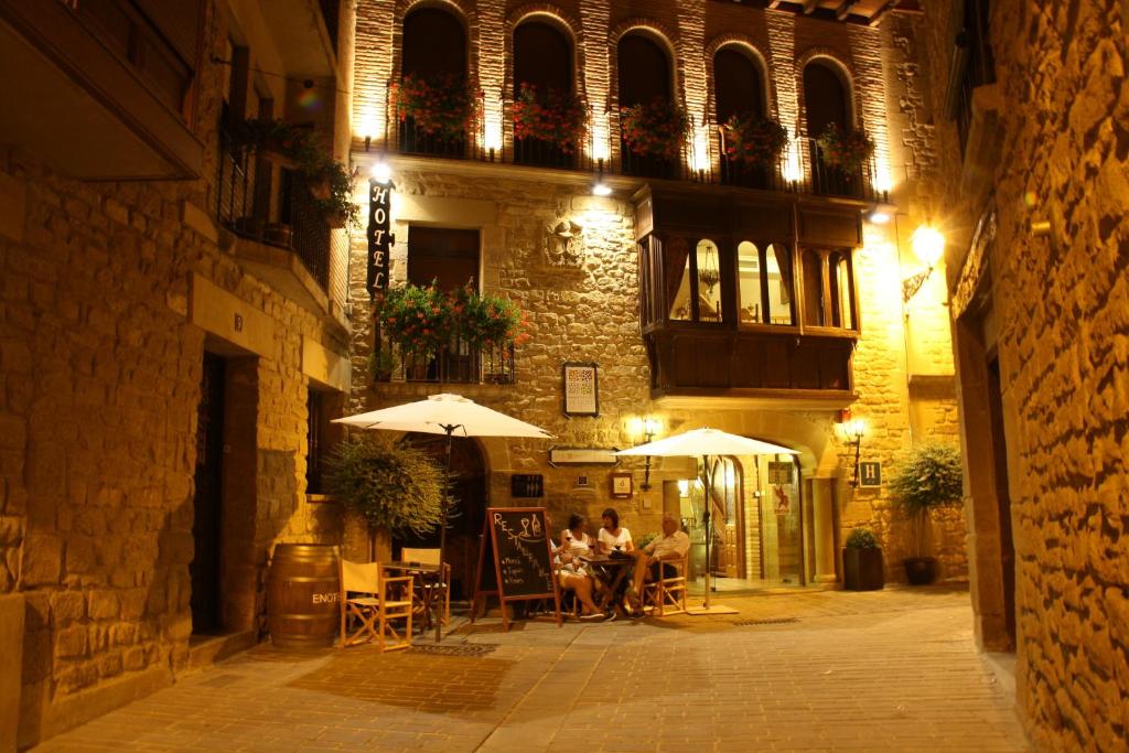 eine Gruppe von Personen, die vor einem Gebäude unter Sonnenschirmen sitzen in der Unterkunft Hotel Merindad de Olite in Olite