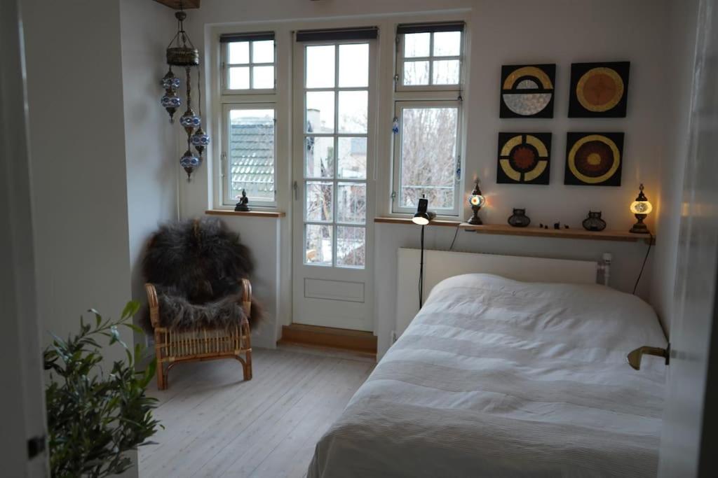 a bedroom with a bed and a chair and windows at villa apartment with sea view in Copenhagen