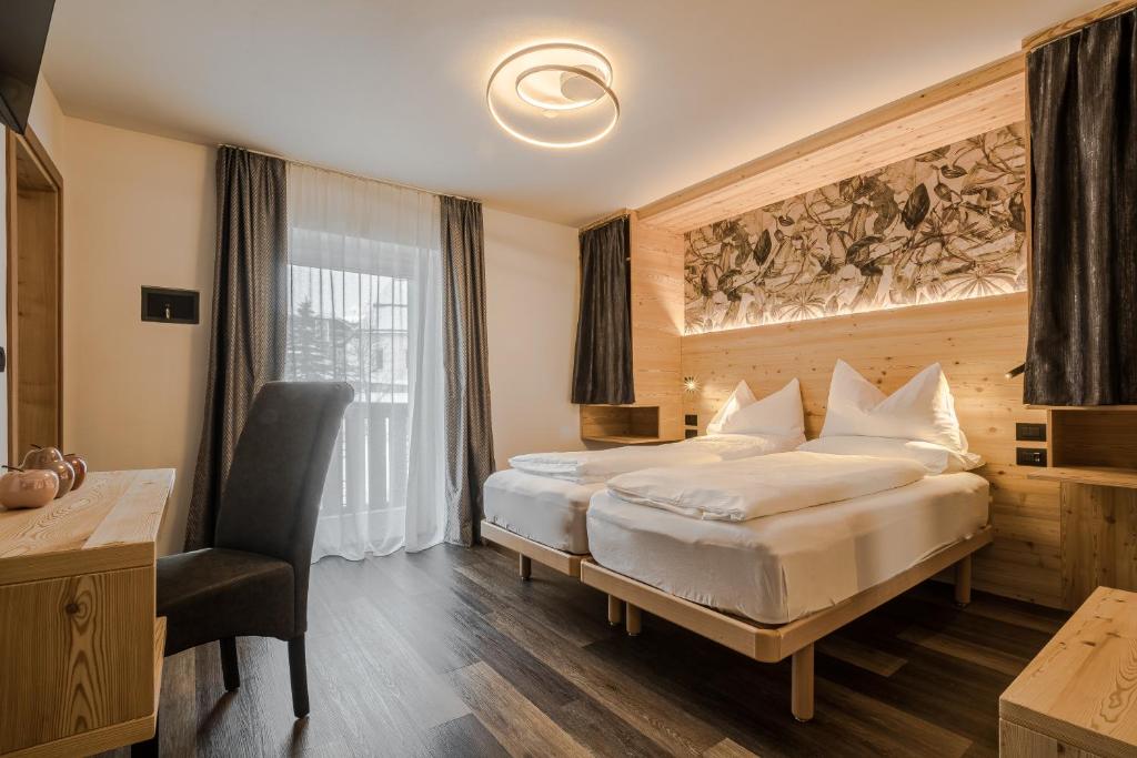 une chambre d'hôtel avec deux lits et une chaise dans l'établissement HOTEL B&B MARILENA, à Arabba