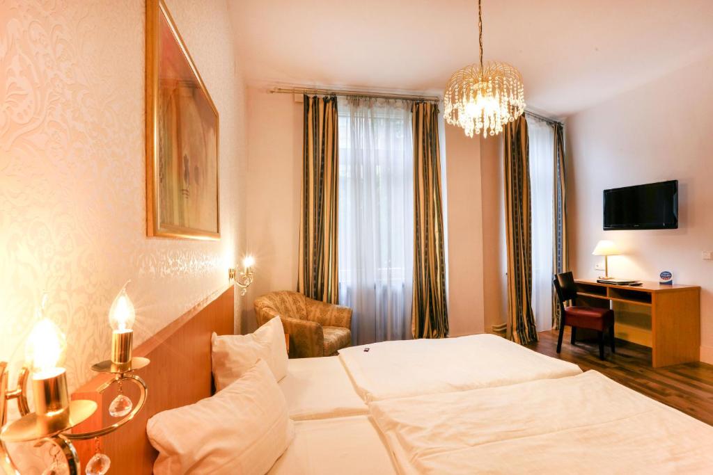 a hotel room with a bed and a desk and a chandelier at Hotel Markgräfler Hof in Karlsruhe