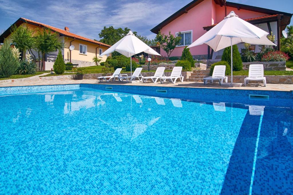 a swimming pool with chairs and umbrellas next to a house at Royal Villas in Bryastovets