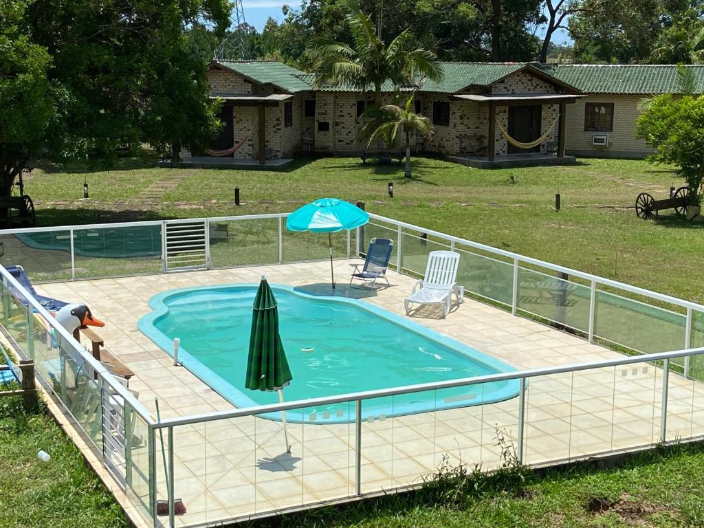uma piscina com um guarda-sol, uma mesa e cadeiras em Pousada Haras Trevo de Ferro, Praia, Piscina e Campo em Torres