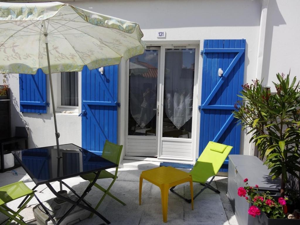 - une terrasse avec des portes et des chaises bleues et un parasol dans l'établissement Charmante maisonnette proche plage et centre-ville, équipée pour 4 pers., parking, WiFi, La Faute-sur-Mer - FR-1-476-105, à La Faute-sur-Mer