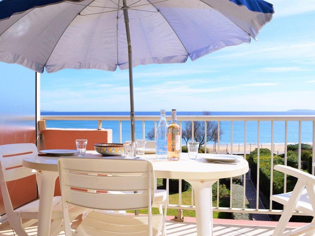 d'une table et de chaises blanches avec un parasol sur le balcon. dans l'établissement Studio au bord de l'eau avec terrasse et ménage inclus - FR-1-251-307, au Lavandou