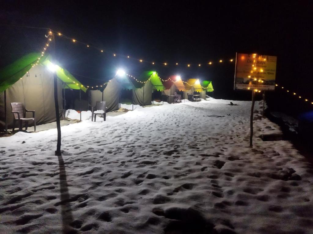 Une rangée de tentes dans la neige la nuit dans l'établissement City Escape Camps and Cafe Kheerganga, à Kheerganga