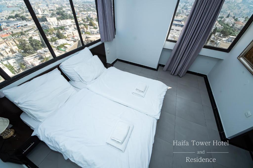 1 cama con almohadas blancas en una habitación con ventanas en Haifa Tower Hotel - מלון מגדל חיפה, en Haifa