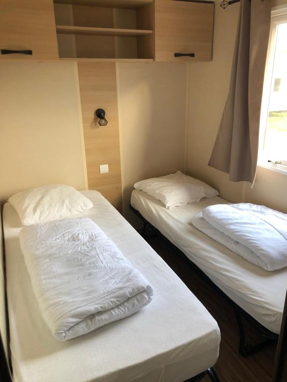 two beds in a room with white sheets and a window at Grand mobil home exposé sud, 2 salles de bain in Onzain