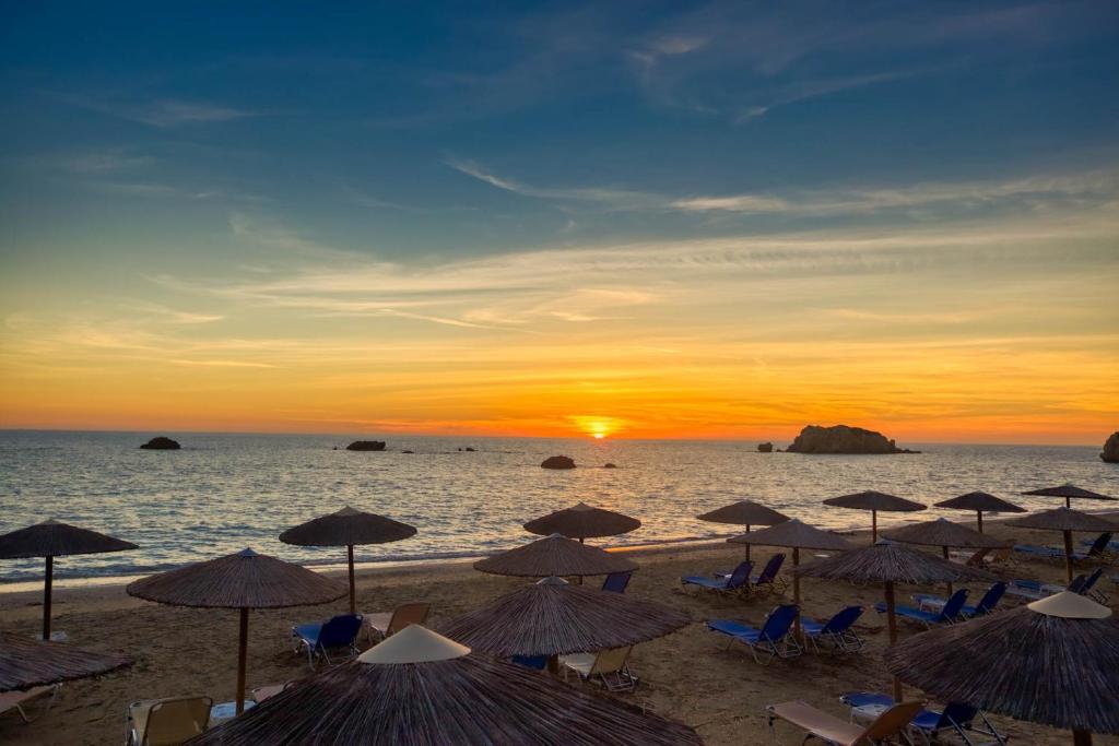 a group of umbrellas on a beach with the sunset at Christinas lofts in Ágios Matthaíos