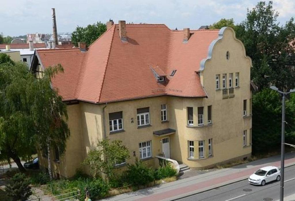 une grande maison avec un toit rouge dans une rue dans l'établissement Udos Gästewohnung, à Cottbus