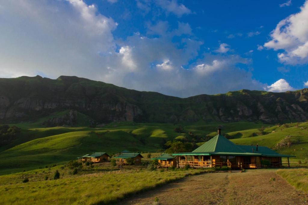 a building in a field with mountains in the background at Greenfire Drakensberg Lodge in Bonjaneni