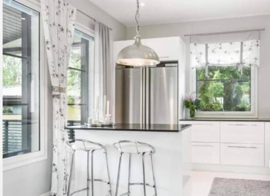 a white kitchen with two bar stools and aandelier at Hienoa talo porealtaalla lähelllä Helsinkiä ja lentokenttää in Tuusula