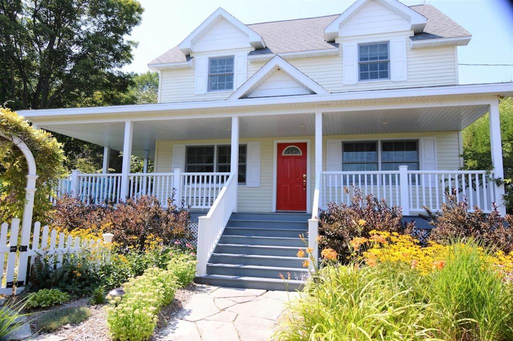 a white house with a red door at Carraig Mor Cottage - Beautiful House, Amazing Garden, Downtown Baileys Harbor in Baileys Harbor