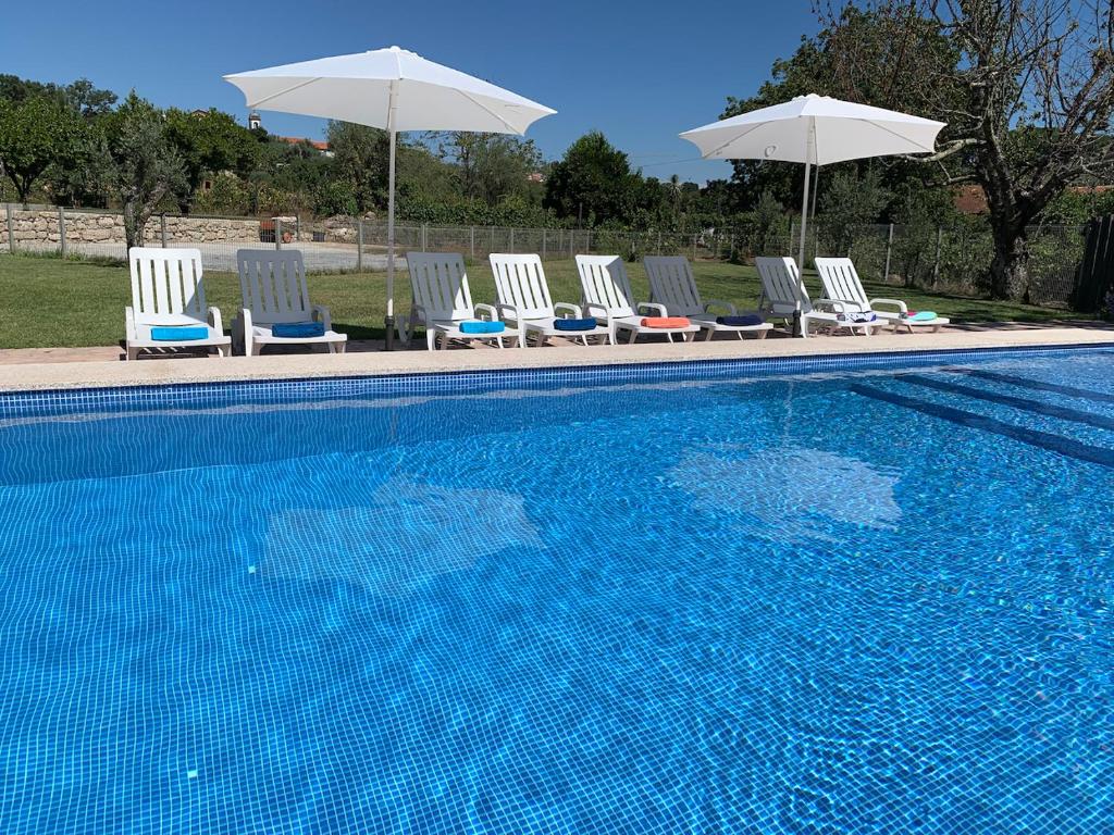 un gruppo di sedie e ombrelloni accanto alla piscina di 6 bedroom countryhouse with pool - Casa do Sepião a Vinhal