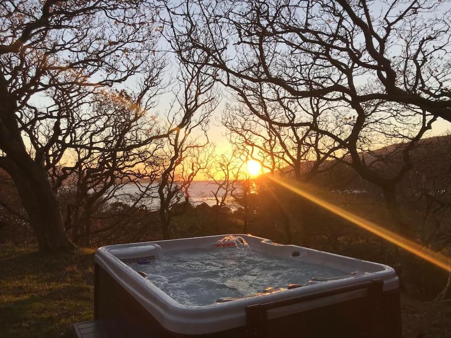 a hot tub in a field with the sunset in the background at Snowdonia Mawddach Cabin + hot tub in Barmouth