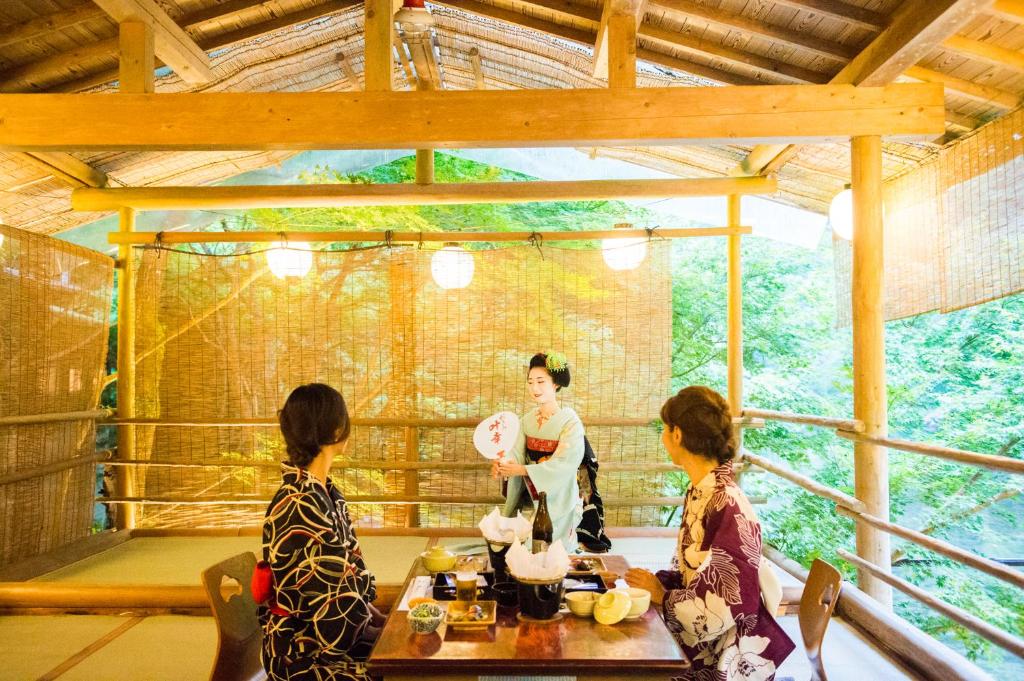 un grupo de tres mujeres de pie alrededor de una mesa en Momijiya Honkan Takaosansou en Kioto