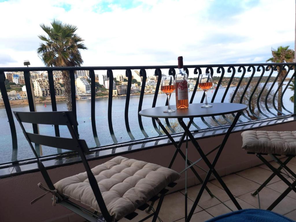 a balcony with a table and two glasses of wine at Seafront Apartment in St. Paul's Bay in St. Paul's Bay