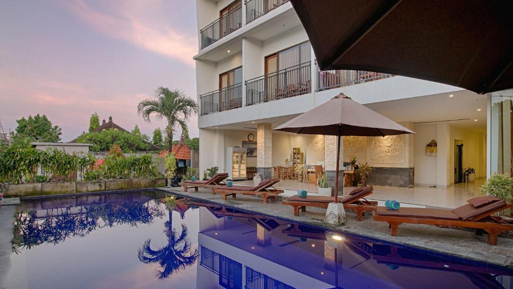 una piscina con sillas y una sombrilla junto a un edificio en My Villa and Resort Canggu, en Canggu