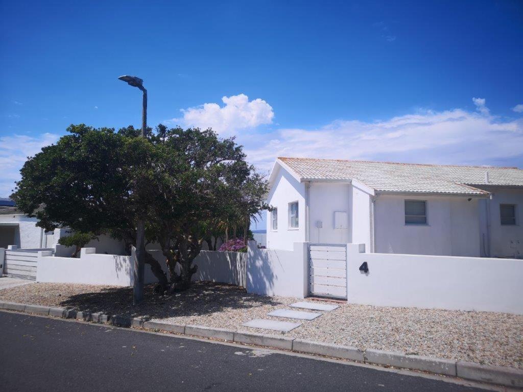 a white house with a tree next to a fence at Barefoot Bungalow in Yzerfontein
