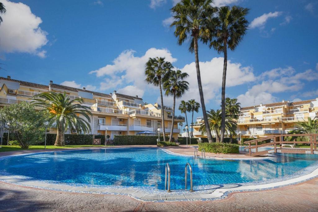 a swimming pool with palm trees in front of a building at Jardines de Denia in Denia