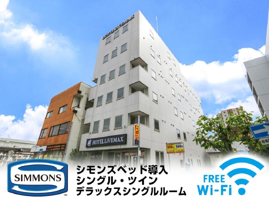 Biały budynek z znakiem przed nim w obiekcie HOTEL LiVEMAX BUDGET Fuji Ekimae w mieście Fudżi