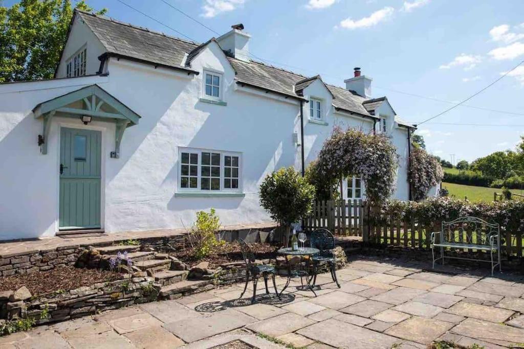 een wit huis met een groene deur en een patio bij Cosy Country Cottage; Brecon Beacons in Crickhowell