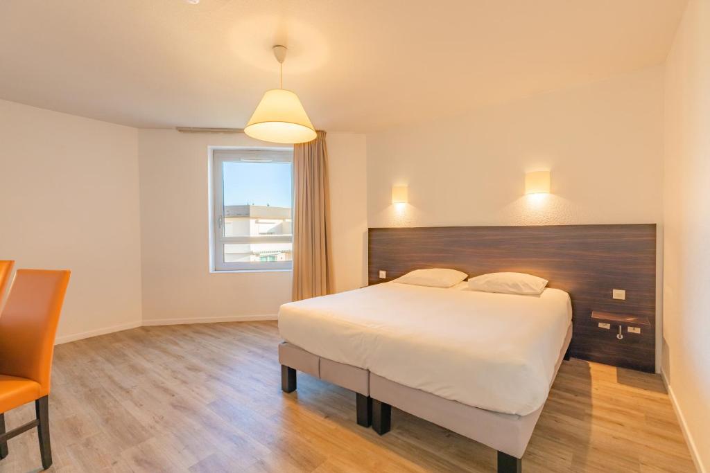 a bedroom with a large white bed and a chair at Appart'City Classic Genève - Gaillard in Gaillard