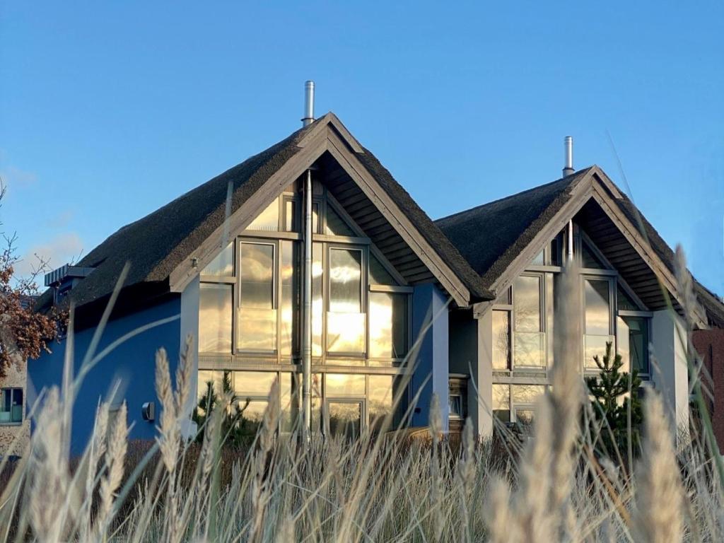 ein Haus mit großen Fenstern auf einem Grasfeld in der Unterkunft Ostsee - Reetdachhaus Nr 2 "SÜDSTRANDHUS" im Strand Resort in Heiligenhafen