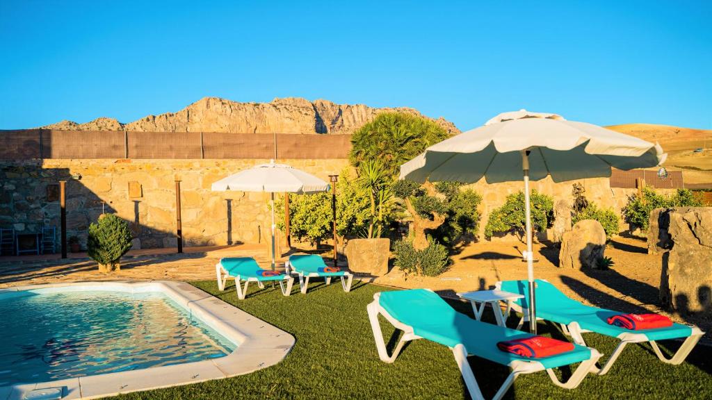 - une piscine avec des parasols, des chaises, une table et des chaises dans l'établissement Casa Rural Los Menhires, à Malaga
