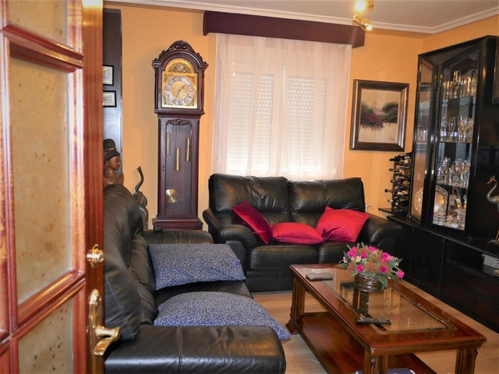 a living room with a leather couch and a clock at Habitaciones en Aviles in Avilés
