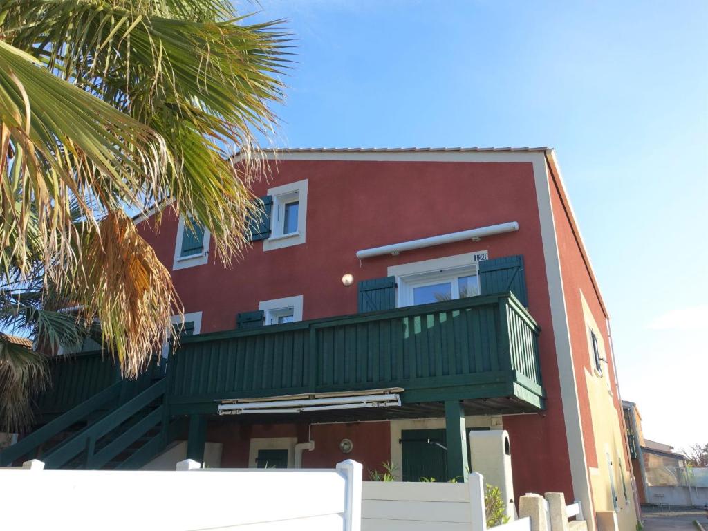 a red building with a balcony and a palm tree at Apartment Eden Roc 2 by Interhome in Narbonne-Plage