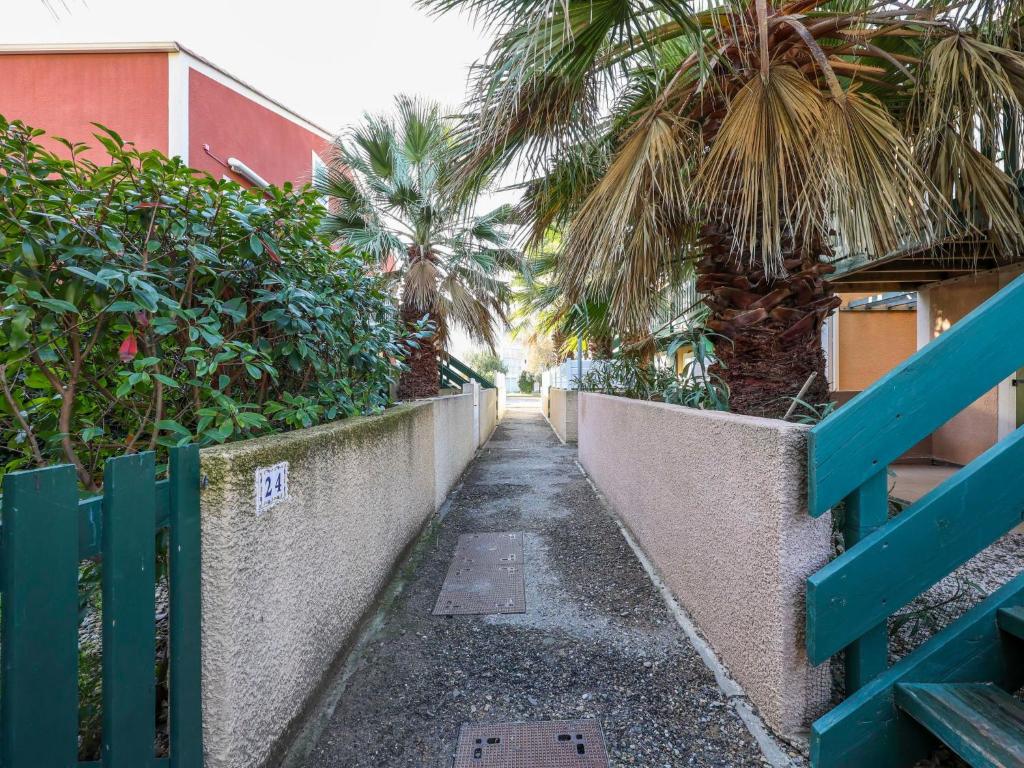 a narrow alley with palm trees and a fence at Apartment Eden Roc 2 by Interhome in Narbonne-Plage