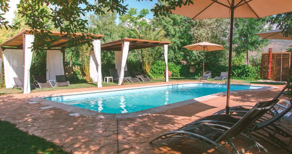una piscina con sillas y sombrilla en El Manantial Del Fresno Casas Rurales En Hervás, en Hervás