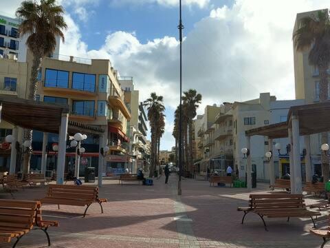 una strada con panchine, edifici e palme di The Clover a San Pawl il-Baħar
