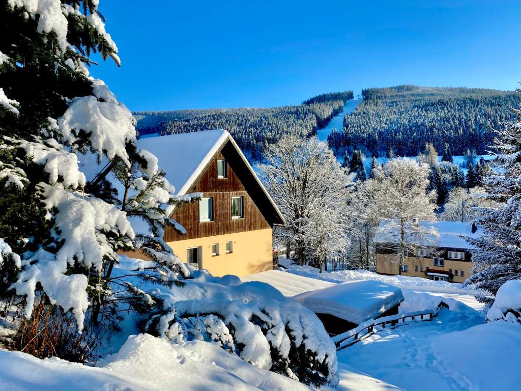 a house covered in snow with a river in the background at Pension Tony in Špindlerův Mlýn