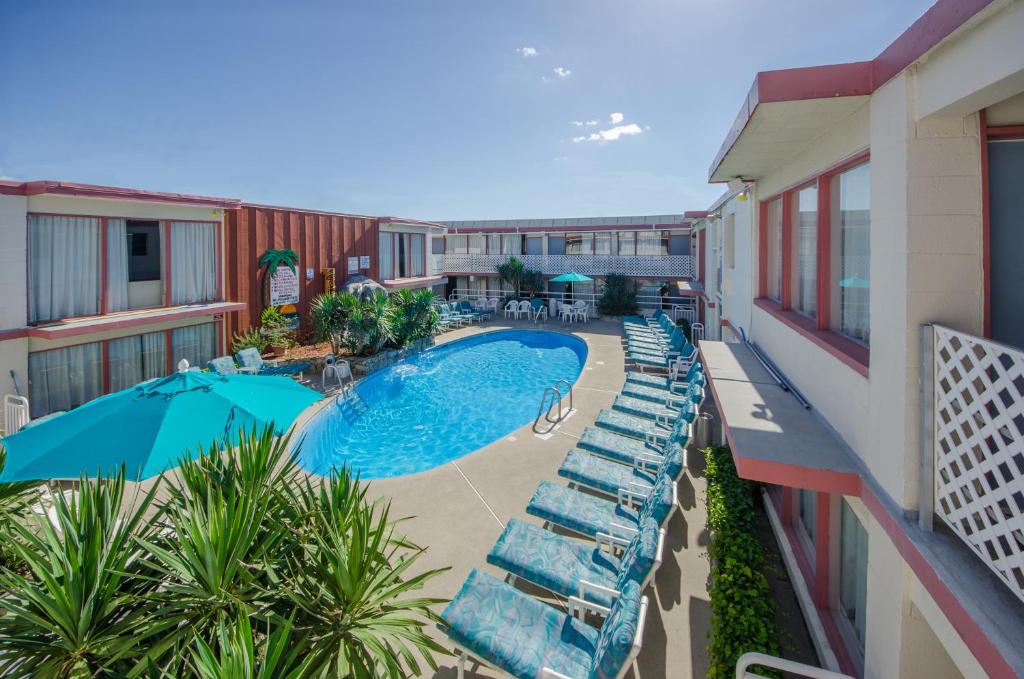 einen Balkon mit Blick auf einen Pool mit Stühlen und einem Sonnenschirm in der Unterkunft Tahiti Inn in Ocean City