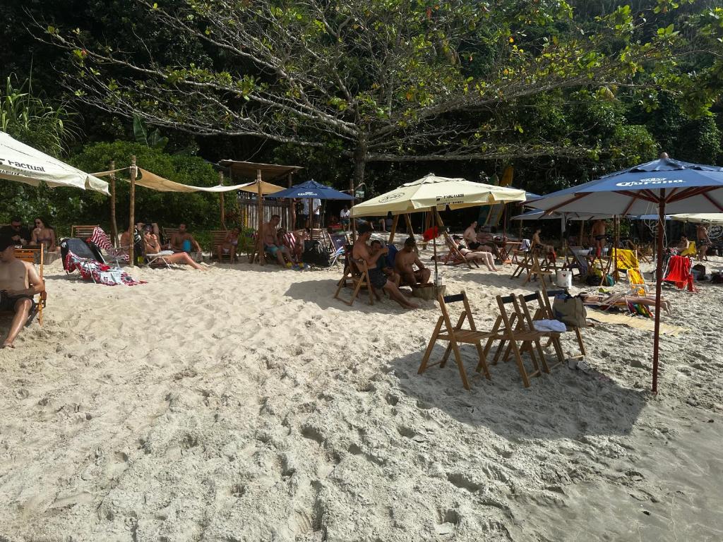 un groupe de personnes assises sur une plage avec des parasols dans l'établissement Casa de boneca em Condomínio - Juquehy, à São Sebastião