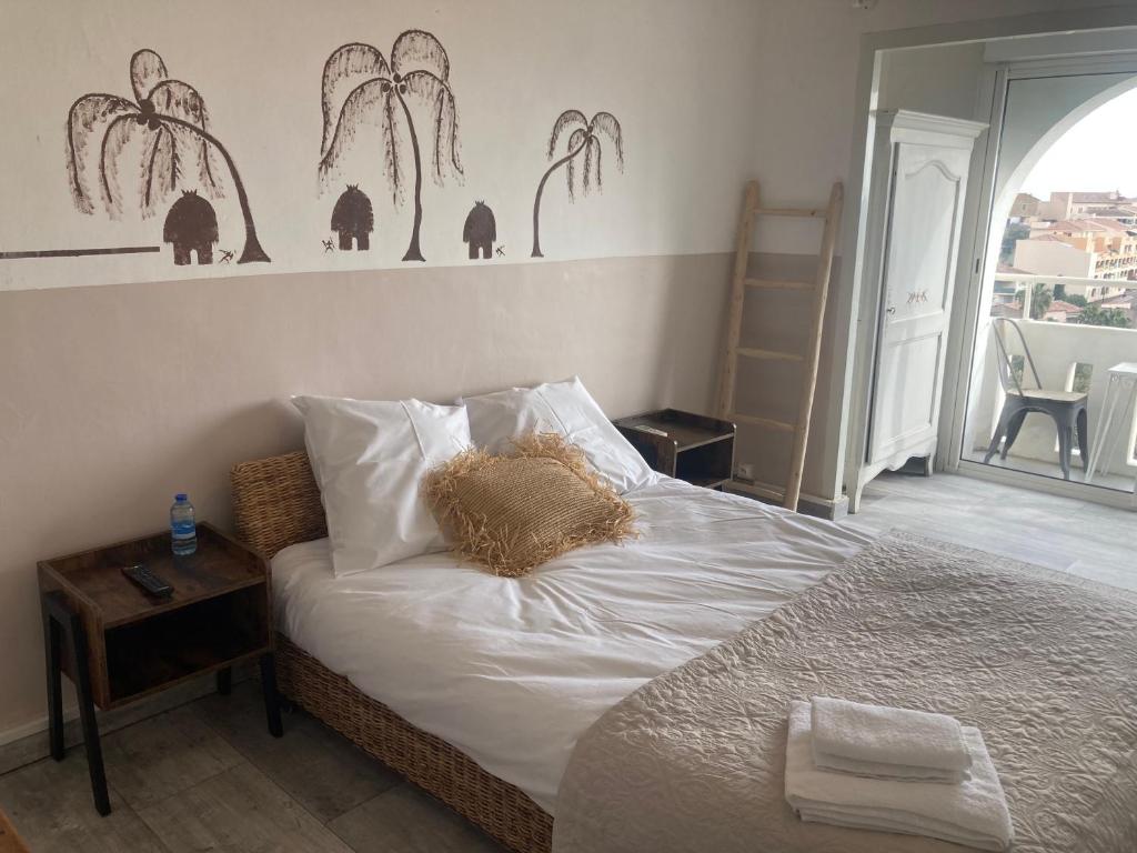 a bedroom with a bed with white sheets and palm trees on the wall at Hôtel Paradis in Bormes-les-Mimosas