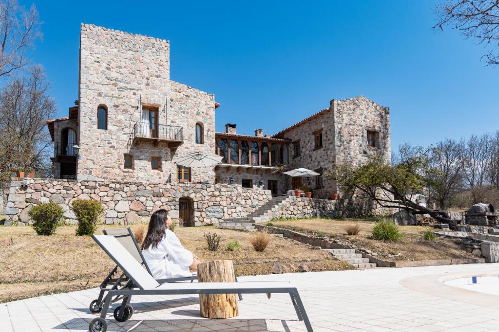 une femme assise sur une chaise devant un bâtiment dans l'établissement Castillo de Piedra Tafi del Valle, à Tafí del Valle