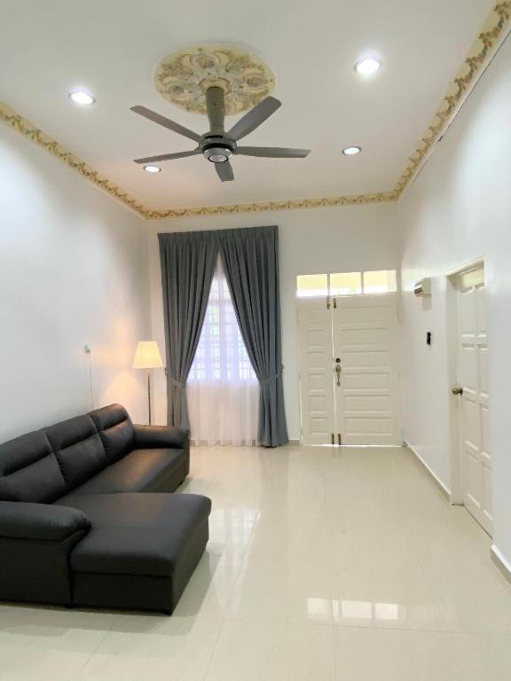 sala de estar con sofá negro y ventilador de techo en Chloe's Homestay, en Kuala Terengganu