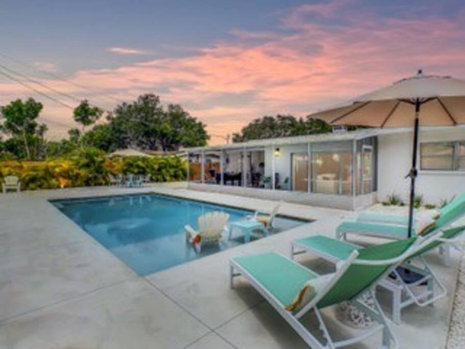 a house with a swimming pool with chairs and an umbrella at The Pink Flamingo Mid Century Heated Pool Paradise in Sarasota
