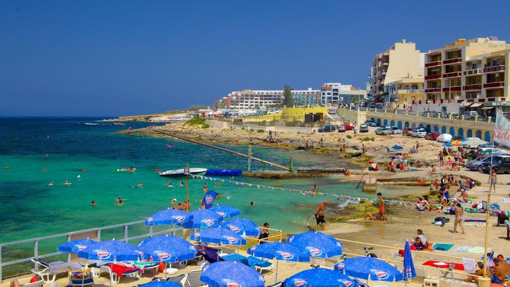 ein Strand mit blauen Sonnenschirmen und Menschen im Wasser in der Unterkunft Sky Apartment 1 in St Paul's Bay